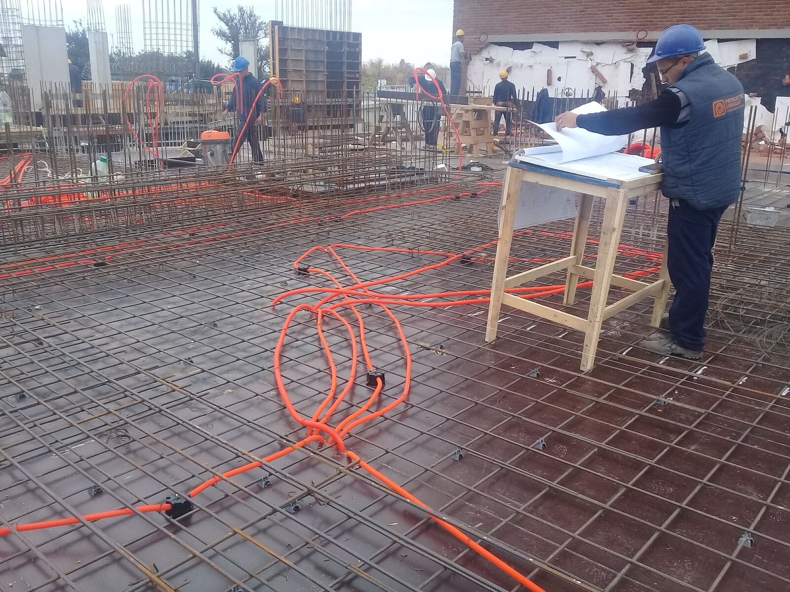 Técnico de Proelectric revisando planos sobre una losa con canalizaciones naranjas